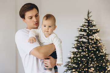 Father holding his baby son near Christmas tree