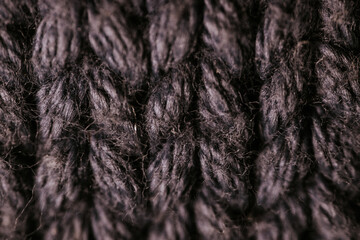 A detailed macro view of dark knitted fabric, showcasing the rich texture and thick yarn weave. The image emphasizes the material's soft and cozy appearance.