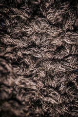 A detailed macro view of dark knitted fabric, showcasing the rich texture and thick yarn weave. The image emphasizes the material's soft and cozy appearance.
