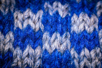 A detailed macro shot of blue and white knitted fabric, showcasing the soft texture and intricate weave of the yarn. The color contrast highlights the artistic pattern.