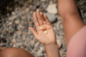 A person is holding a handful of nuts in their hand. The nuts are of different sizes and shapes, and they appear to be almonds. The person seems to be enjoying the nuts and is likely to eat them soon.