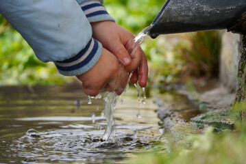 Varna, Bulgaria - 03.12.2023: A small child washes his hands in running water from a fountain in the forest. Emotion of crystal water.