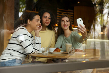 Women taking selfie at coffee meeting in cafe, view through window