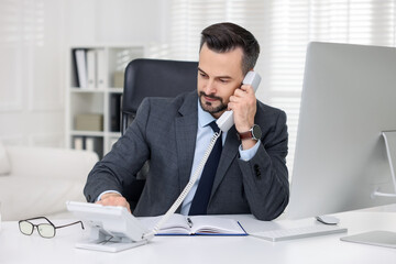 Naklejka premium Handsome banker talking on phone at table in office