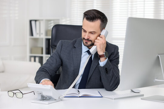 Handsome banker talking on phone at table in office
