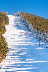 Hruby Jesenik, Snow-covered ski slope on the mountain slope with chairlift ski lift, view from the hiking trail during winter hiking in the mountains, winter landscape in the mountains.