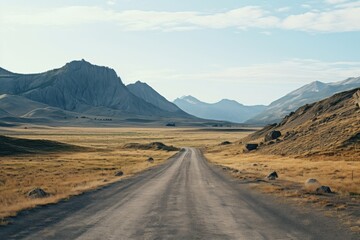 Fototapeta premium Scenic dirt road winding through expansive grassy plains and rocky mountains during the day