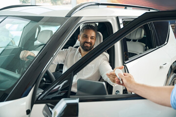 Happy young man receiving car key from salesman