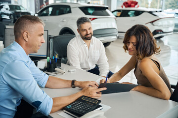 Couple buying new car in auto salon, signing contract