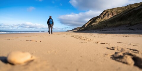 Obraz premium A person strolls along a tranquil beach, flanked by towering cliffs under a vibrant blue sky, capturing the essence of solitude and natural beauty by the sea.