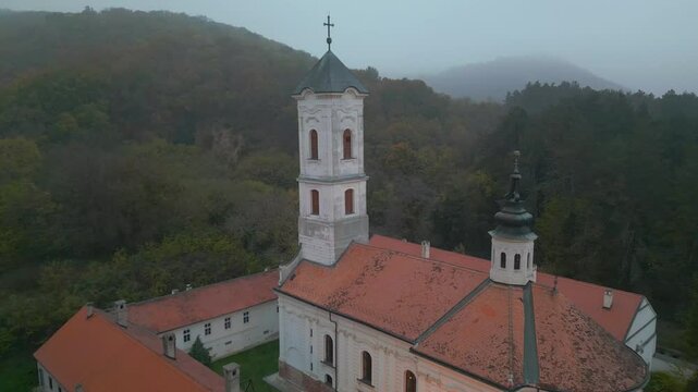 Mystical aerial view of Vrdnik Ravanica monastery in thick fog, historic Serbian Orthodox church and famous travel destination in Fruska Gora, Serbia, 4K drone