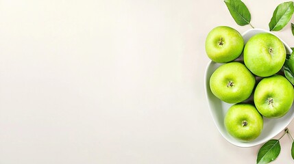   A white bowl holds green apples on a light-colored tablecloth, accompanied by a leafy branch