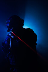 Fototapeta premium Silhouette of a Tactical Soldier with Red Laser Backlit in Fog