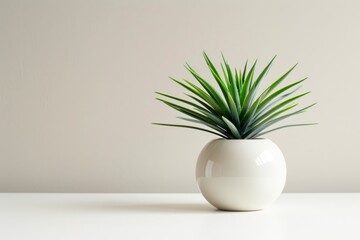 A vibrant green artificial plant in a minimalist white spherical pot sits on a white surface against a light beige wall.