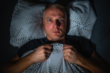 Mann liegt wach und mit ängstlichem Gesicht nachts im Bett