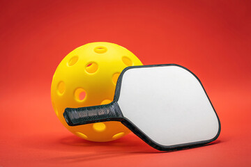 Close up of Yellow Pickleball with white Pickleball Paddle on a red background.