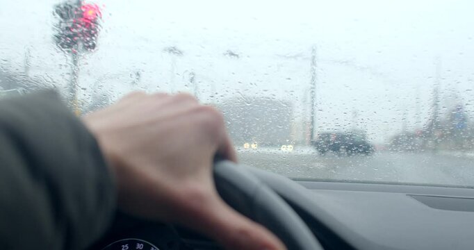 My hand grips the wheel firmly as the rainsoaked windshield shows a red traffic light behind