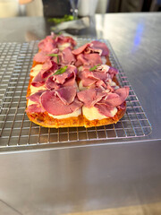 Rectangular pizza with smoked meat ham and pastrami on wire rack