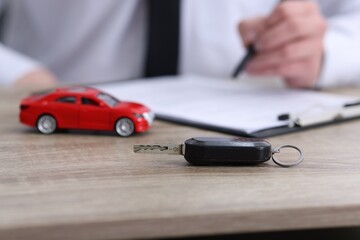 Man signing car purchase agreement at wooden table, focus on key. Buying auto