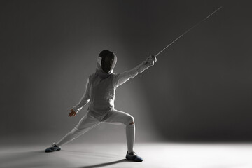 Fencer with epee practicing on gray background