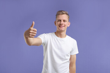 Fototapeta premium Happy man showing thumbs up on purple background. Like gesture