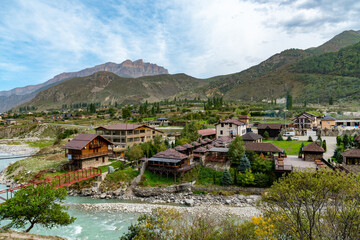 A modern tourist village in the middle of the mountains next to a fast mountain river. Background of mountain meadows and blue sky with clouds