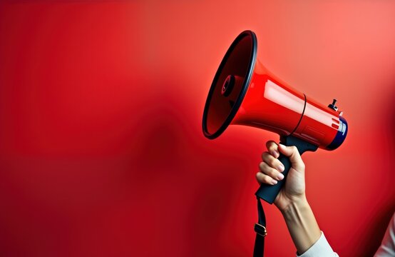 Woman confidently holds red megaphone against bold red background. Powerful communication concept. Ideal for important announcement marketing campaign. Simple design. Empty space available for custom
