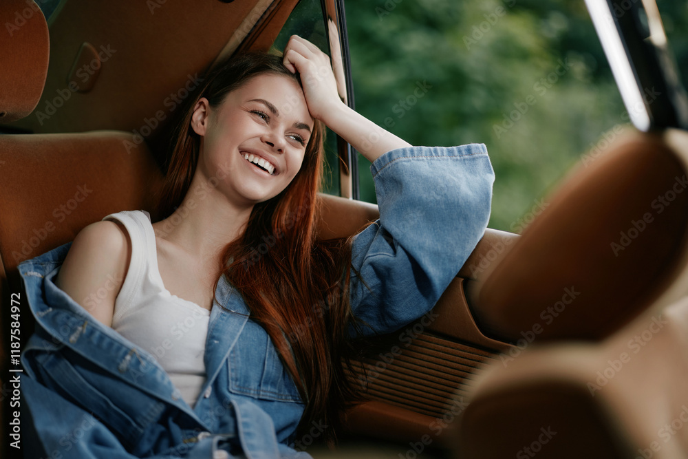 Canvas Prints Young woman with long red hair smiling in a denim jacket sitting in a car, enjoying a sunny day outdoors, showcasing warmth and happiness.