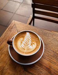 A cup of coffee with intricate latte art in the shape of a leaf sits on a rustic wooden table, showcasing the skill of the barista. Generative AI