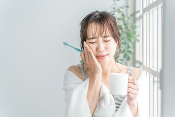 虫歯が痛い・しみて頬を押さえるアジア人女性
