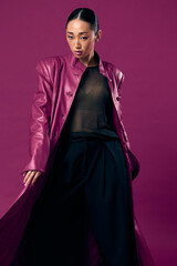 Naklejka premium Fashion asian woman wearing a purple leather coat and black pants posing with eyes closed against a purple background