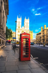A classic red telephone booth on a London street, perfectly framed by the historic Westminster Abbey in the background. This image captures the essence of British heritage, blending traditional 