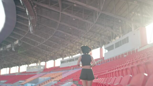 A woman runs in a stadium with a red and blue background. The stadium is empty and the woman is the only person in the scene