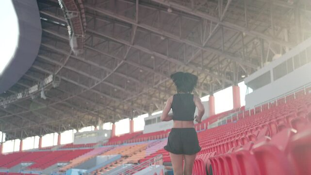 A woman runs in a stadium with a red and white background. The stadium is empty, and the woman is the only person in the scene