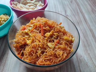 A bowl of stir-fried vermicelli with eggs, carrots, and spices, served on a wooden table. Perfect for showcasing Asian cuisine, home cooking, or food styling concepts.