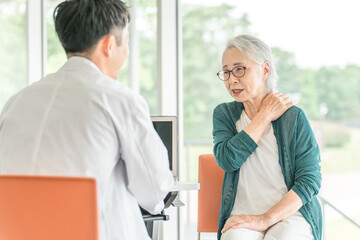 Fototapeta premium 肩こり・肩を痛がるシニア女性と診察する男性医師の後ろ姿 