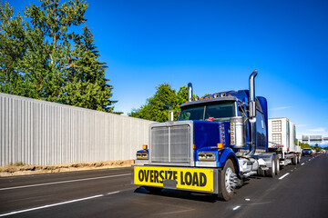 Bright blue big rig semi truck with oversize load sigh on the front bumper transporting oversized...