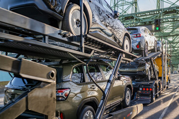 Car hauler yellow big rig semi truck transporting cars on the two level hydraulic semi trailer running on the road with truss arched bridge