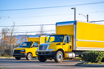 Middle duty bright yellow day cab big rig semi trucks with box trailers standing on the parking lot...