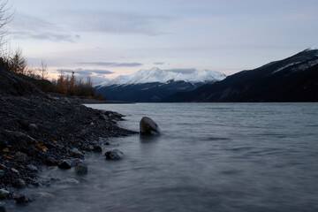 Rocks on the shore of Muncho lake with a mountain in the background on a cold autumn morning in Canada.