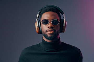 Obraz premium Stylish Black man wearing headphones and sunglasses, exuding confidence against a colorful gradient background, perfect for music and fashion themes