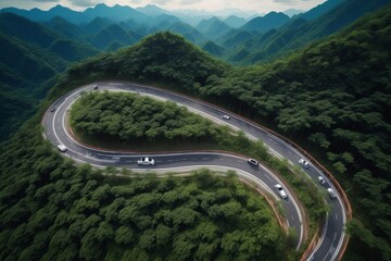 Aerial view of a winding mountain highway with cars surrounded by lush green trees and a river crossing under a bridge