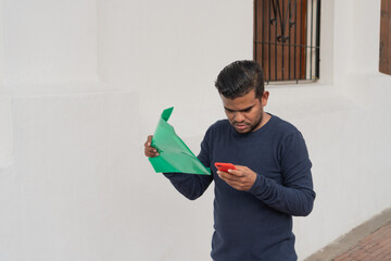 Latino man reading documents and using smartphone on a city street