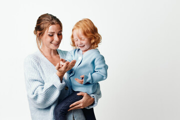Happy mother with child in arms smiling at camera in white background, family love and joy concept