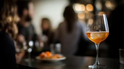 A vertical shot of a drink in a wine glass on the table with a blurred people in the background