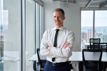 Fototapeta premium Smiling confident young business man looking at camera, portrait. Happy professional businessman executive ceo manager, rich male entrepreneur company owner wearing tie standing crossed arms in office