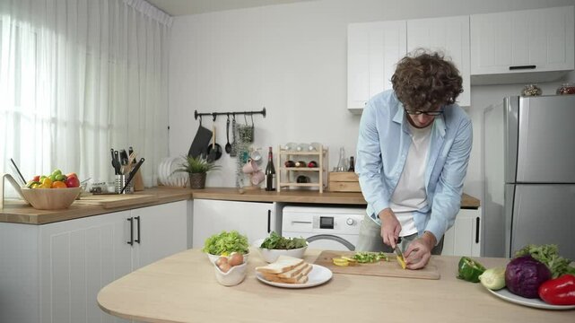 Happy father move to music while cooking food and prepare lunch at modern kitchen. Active dad dancing to song while making healthy food or salad surrounded with vegetable and kitchenware. Pedagogy.