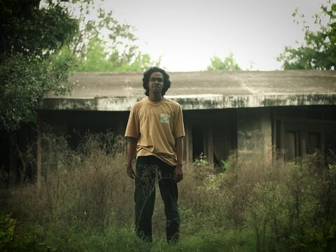 A boy standing in a forest with an old abandoned house behind him at aravali hills
