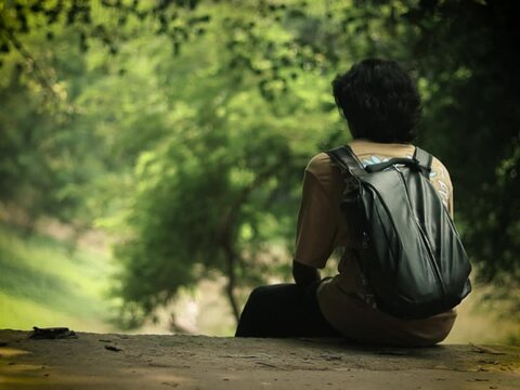A boy seating in a midst of aravali forest wearing a black bag on his back

