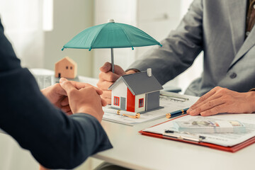 An insurance agent's hand holds an umbrella over a small house. Symbol of life insurance and home...